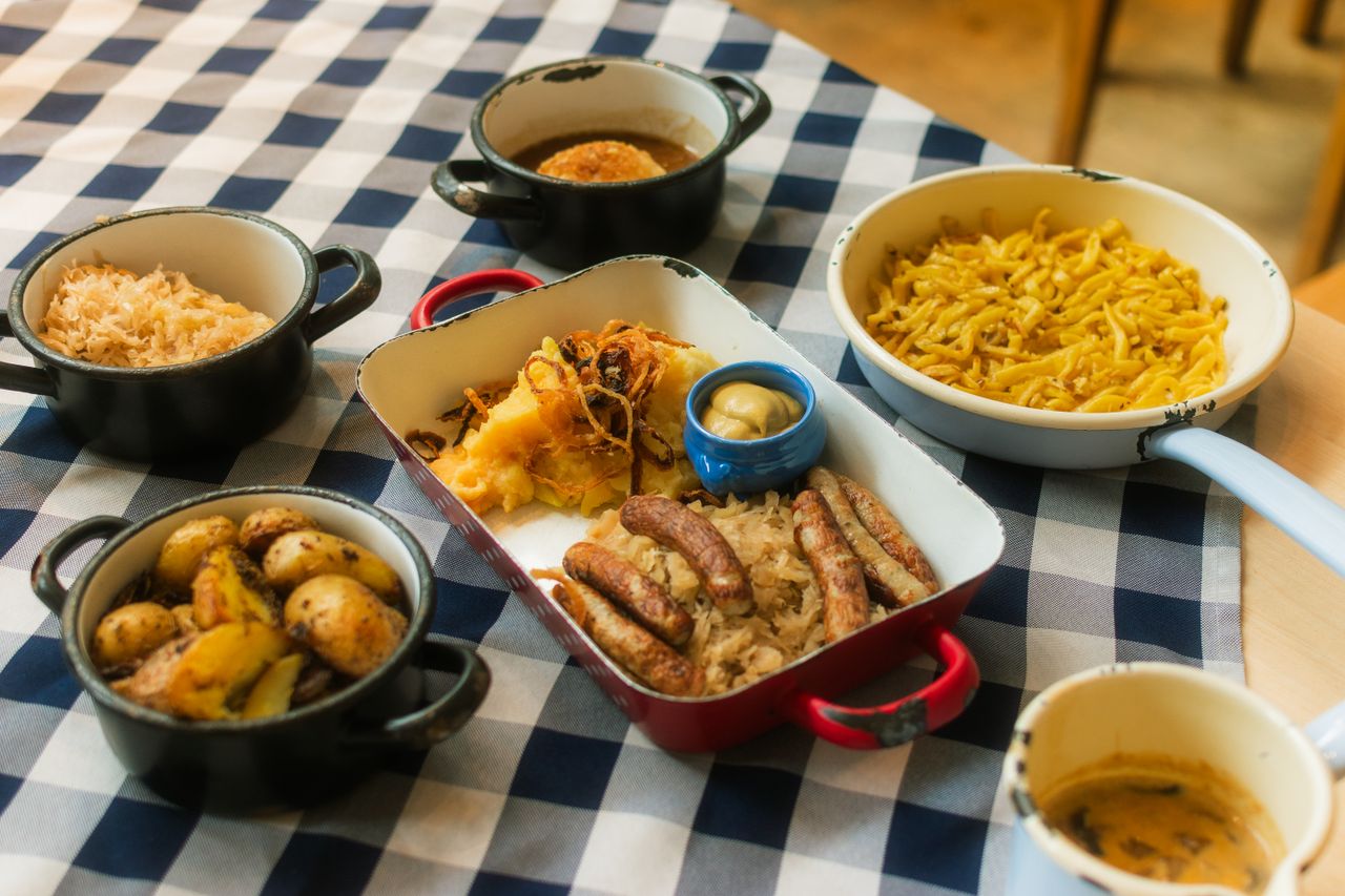 A delicious assortment of German cuisine featuring sausages, potatoes, sauerkraut, and more on a checkered tablecloth.