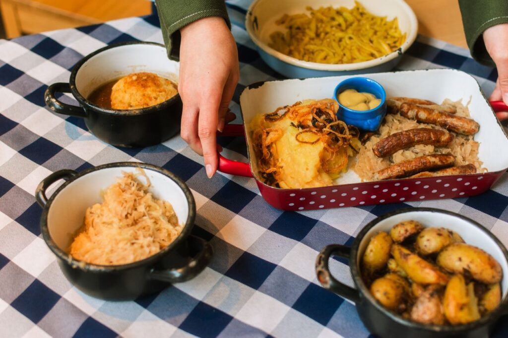 Traditional Bavarian meal with sausage, sauerkraut, potatoes, and gravy on a checkered tablecloth.