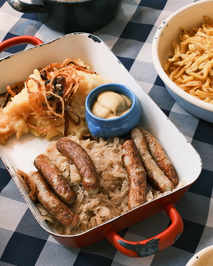 Delicious German sausages served with sauerkraut, mashed potatoes, and mustard on a blue checkered tablecloth.